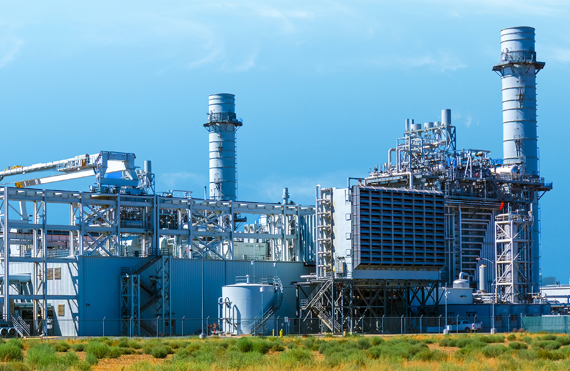 Industrial power plant with large chimneys and metal structures under a clear sky.