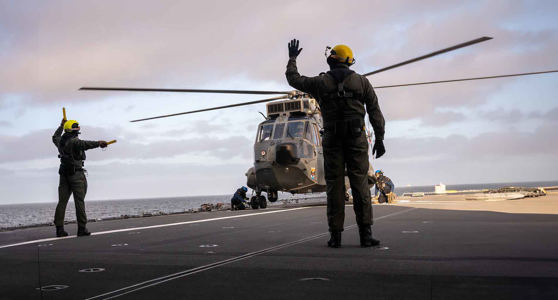 Helicopter landing on aircraft carrier deck with crew directing the pilot.