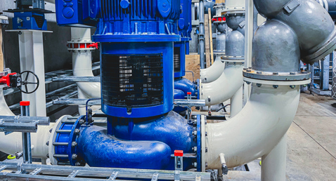 Alt text: Array of blue DESMI DSL double-suction pumps used for temperature regulation in a power-to-x plant, connected to large white process piping, valves, and fittings in an industrial facility.