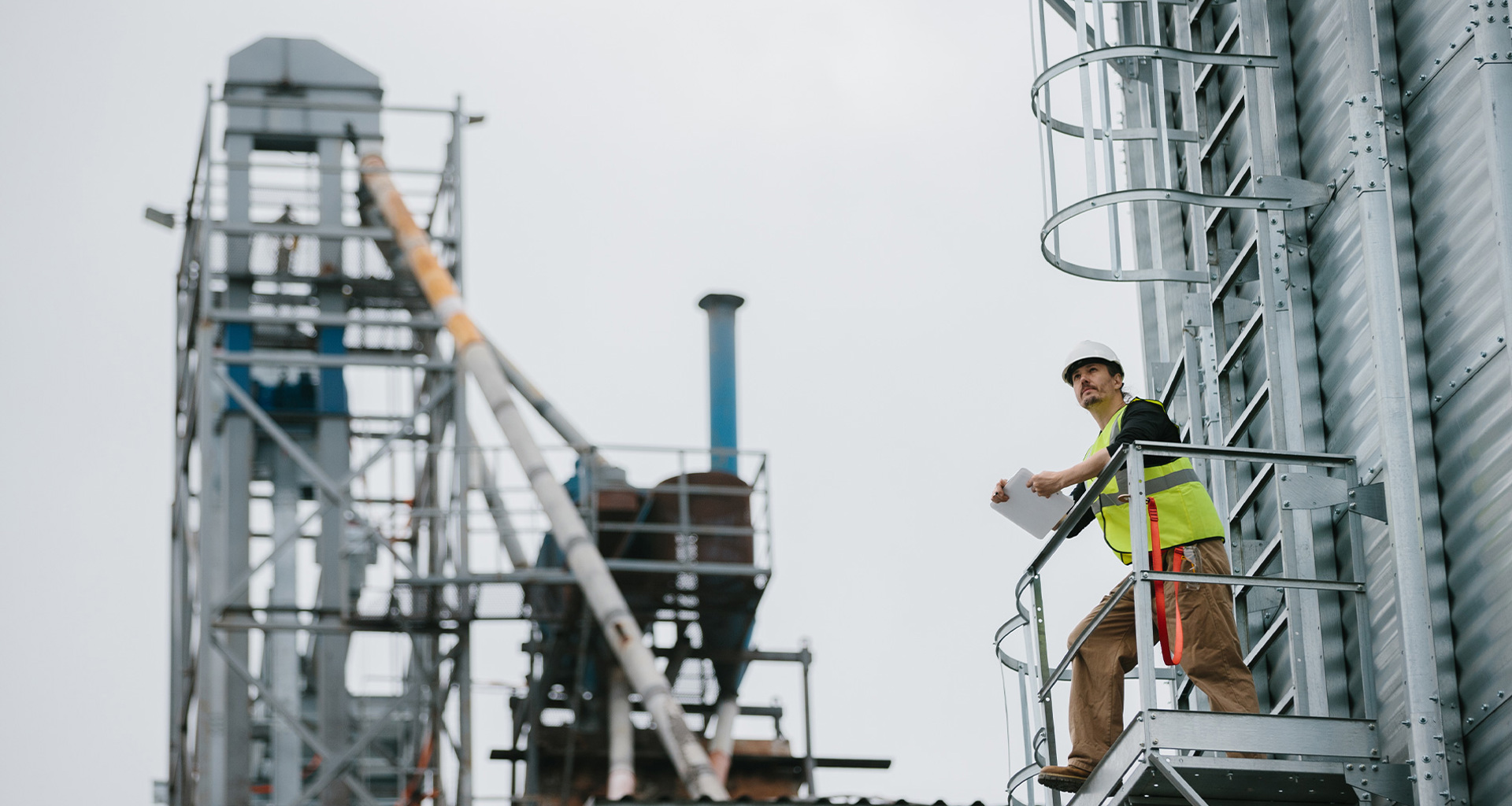 Construction worker in safety gear inspects industrial site from elevated platform.