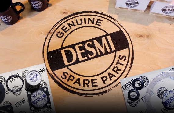 DESMI genuine spare parts on a wooden surface with branded mugs and packaging.